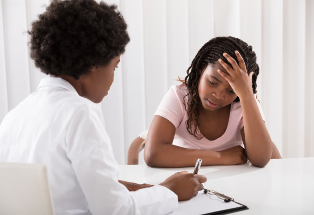 A woman in a pink shirt consults with a doctor in a white coat, discussing her concerns at a medical appointment.