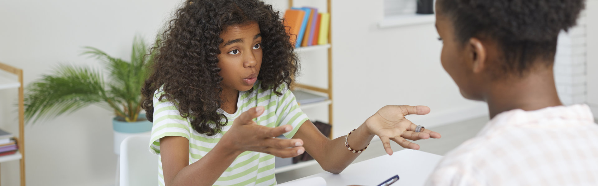 A therapist listens attentively to a young girl expressing herself during a counseling session in a bright office.