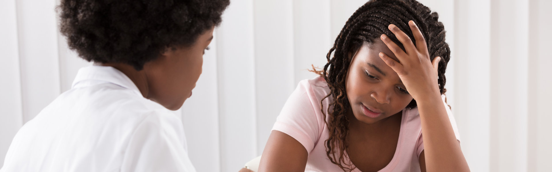 A woman in a pink shirt consults with a doctor in a white coat, discussing her concerns at a medical appointment.